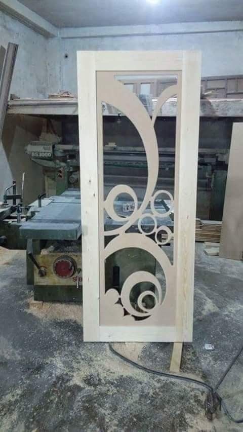 Decorative Wooden Door Panel with Intricate Swirl Cutouts in Workshop