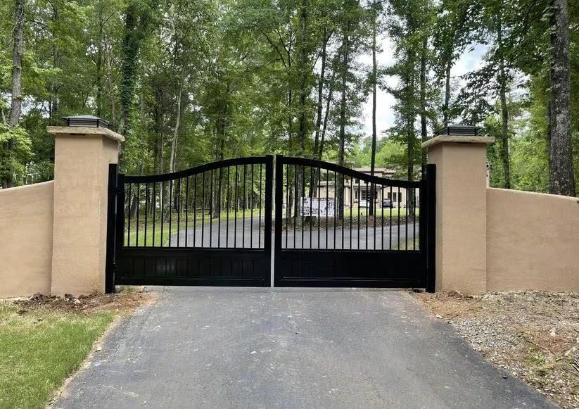 Modern Black Iron Driveway Gate with Stucco Pillars in Wooded Setting